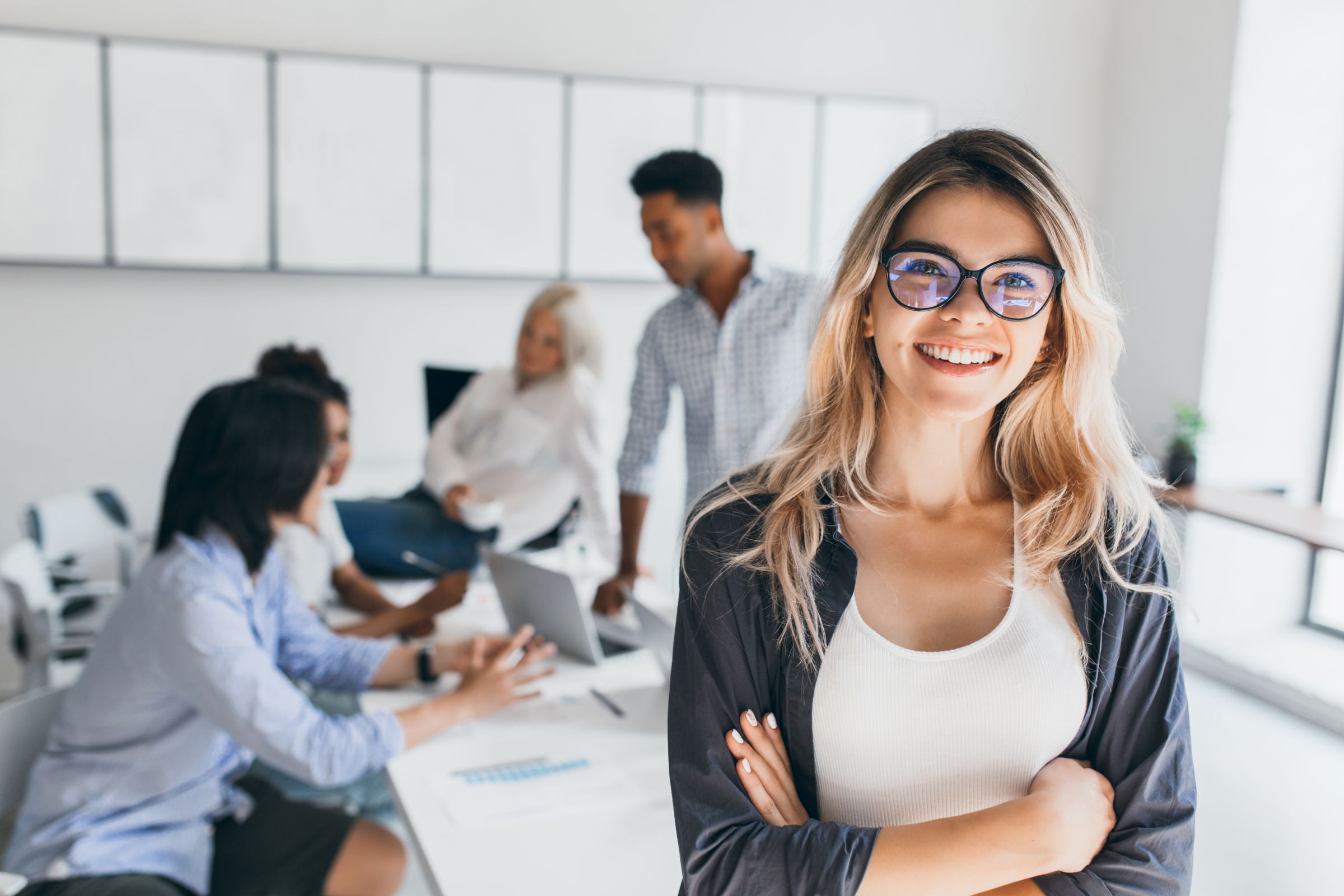 Blonde Female Executive Posing With Smile Arms Crossed During Brainstorm With Managers Indoor Portrait European Student Spending Time Hall With Asian African Friends